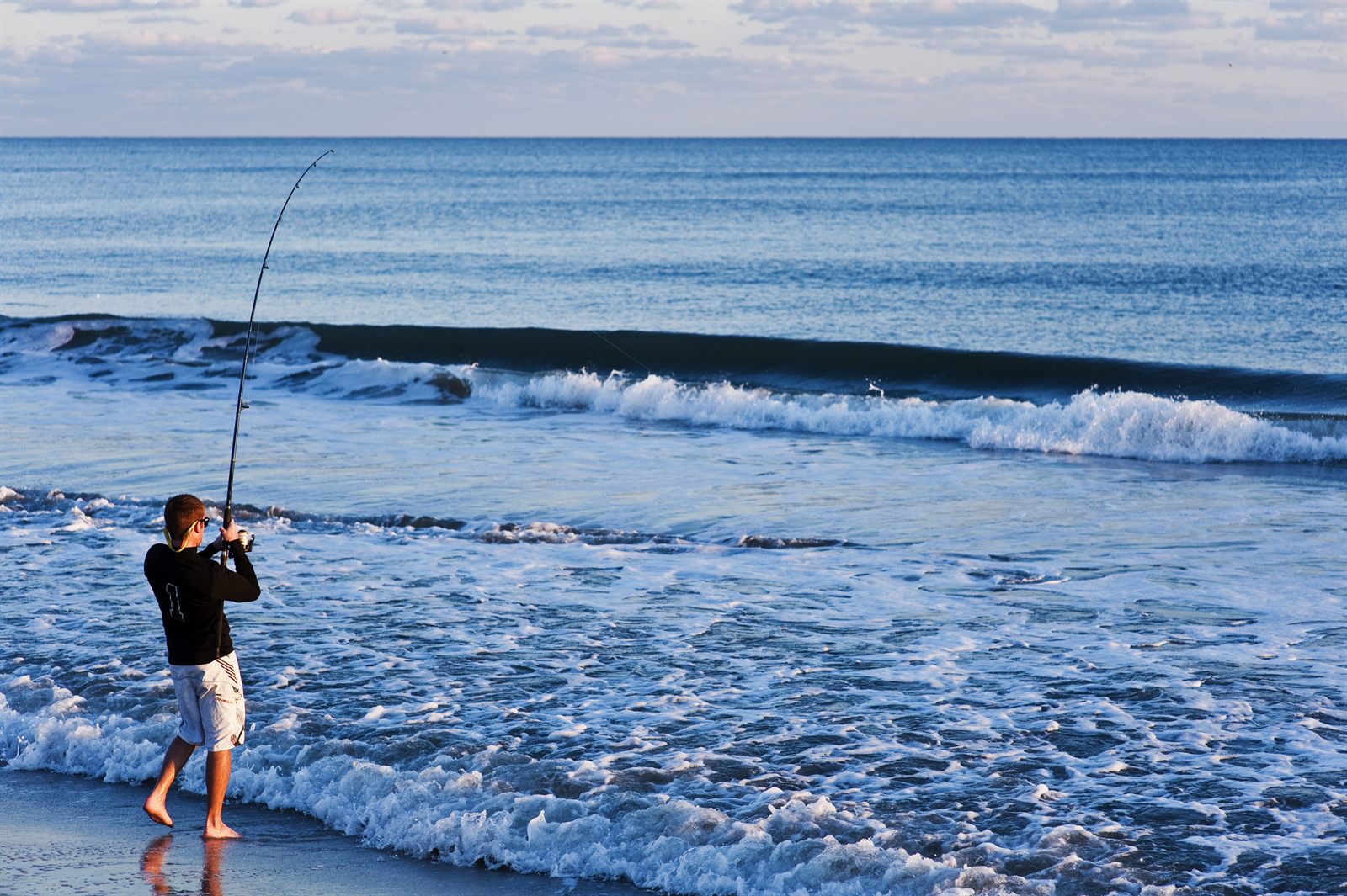 An angler casting into the surf from an Atlantic beach in early light, one of the classic things to do on the Treasure Coast, Florida